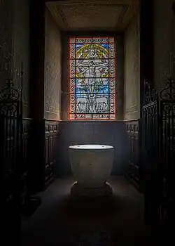 Le baptistère. Sur le vitrail est représentée la crucifixion de Jésus avec en arrière-plan, Dieu le Père soutenant la croix.