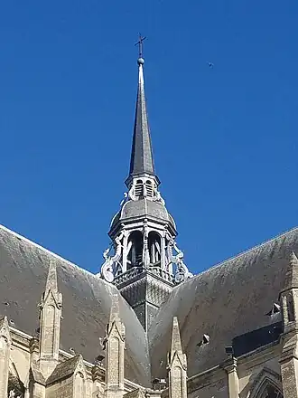 Grande flèche de bois surmontée d'une croix. En arrière-plan, un ciel bleu avec un oiseau.