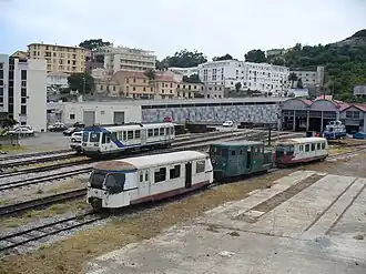 Vue des voies du dépôt avec motrice X 97050, 2 remorques blanches "Billard" réformés, "la bête de Calvi" tracteur n° 114 au milieu, Bâtiment administratif à étages à gauche. A droite remises à autorails et atelier.