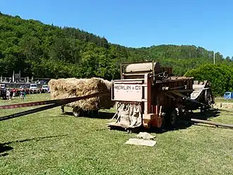 Batteuse Merlin (vers 1950). Vue sur l'ensachage des grains. La courroie sur le flanc de la machine entraîne une presse  séparée à  l'arrière.