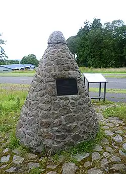 Photographie d'un empilement de pierres de forme conique sur lequel est fixée une plaque de couleur noire