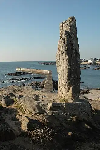 Vue d’un menhir avec en arrière plan une digue et la mer.