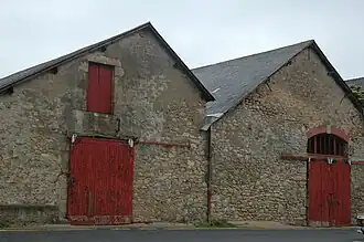 Vue de deux bâtiments en pierre jumelés, aux boiseries rouges closes.