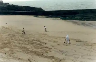 Photographie de trois hommes en combinaison blanche sur une plage.