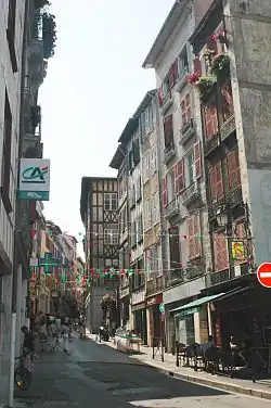 Vue d’une rue de bâtiments de 3 et 4 étages, aux façades blanches à pans de bois peints.