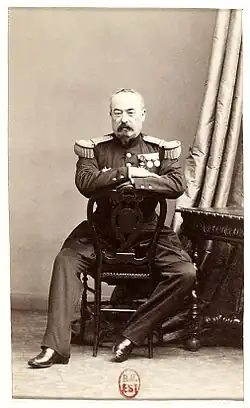 Photographie d'un officier militaire posant assis sur une chaise retournée.