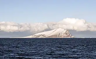 Île montagneuse enneigée avec deux icebergs au loin.