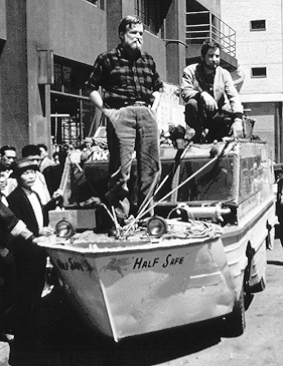 Deux hommes debout, sur un véhicule amphibie, au milieu d'une foule.