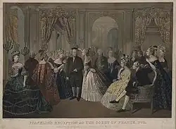 Gravure en couleurs représentant Louis XVI et Marie-Antoinette, assis regardant Franklin qu'une dame de la cour pare d'une branche de laurier, en présence de plusieurs courtisans.