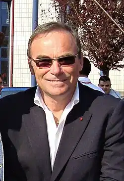 Photographie d'un homme vêtu d'une chemise blanche, d'une veste noire et porteur de lunettes de soleil