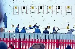 Un athlète couché vise une des sept cibles présentes sur la photo.