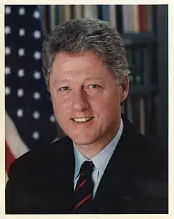 Portrait officiel en couleurs d'un homme aux cheveux grisonnants, en vue poitrine. Il porte une veste noire et une cravate et se trouve devant un drapeau des États-Unis.