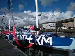 Plan rapproché sur les foils rouges d'un voilier bleu sombre et bleu clair amarré au ponton.