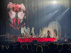 Image d'un concert théâtralisé avec plusieurs musiciens devant un public
