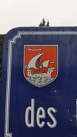 Photo d'une représentation du blason sur un panneau indiquant le nom d'une rue de la commune.