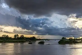 Nuages bleus et orange au-dessus du Mékong avec une pirogue filant sur l'eau au coucher du soleil à Don Det.