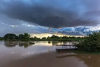 Nuages bleus orageux au-dessus du Mékong au coucher du soleil avec réflexion dans l'eau et une pirogue amarrée à la berge, à Don Det.