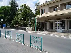 Vue d’un poste de douane, au bord d’une route, bâtiment blanc à un étage.