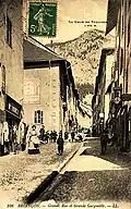 Carte postale ancienne présentant la grande rue et la grande gargouille (au centre de la chaussée)