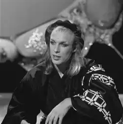 Portrait en noir et blanc de Brian Eno avec des cheveux longs surmontés d'un béret