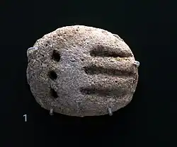 Petite tablette arrondie comprenant des signes ronds et linéaires.