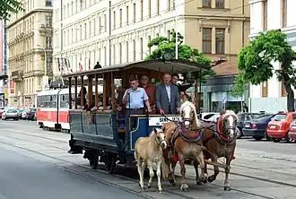 Omnibus hippomobile tracté par deux chevaux dont l'un est accompagné d'un poulain.