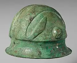 Casque antique en bronze vert patiné, décoré, centré sur fond gris uni.