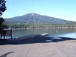 Un parking, un lac bordé d'une forêt derrière, et une montagne qui est légèrement inclinée dans l'arrière-plan.
