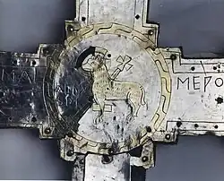 Photo d'un dessin en aplats dorés et au trait noir d'un agneau avec une auréole autour de la tête et une crosse derrière lui.