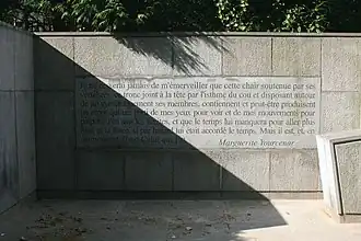 Citation gravée dans la pierre : "Je ne cesserai jamais de m'émerveiller que cette chair soutenue par ses vertèbres, ce tronc joint à la tête par l'isthme du cou et disposant autour de lui symétriquement ses membres, contiennent et peut-être produisent un esprit qui tire parti de mes yeux pour voir et de mes mouvements pour palper… J'en sais les limites, et que le temps lui manquera pour aller plus loin, et la force, si par hasard lui était accordé le temps. Mais il est, et, en ce moment, il est Celui qui Est. - Marguerite Yourcenar"