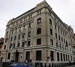 Photographie d'un bâtiment aux pierres jaunes, arborant un drapeau à plusieurs croix blanches, rouges et bleues entrecroisées.