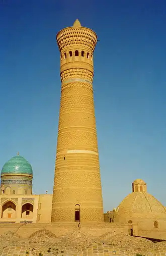 Un grand minaret,avec des structures en forme de dôme et un ciel bleu derrière lui.