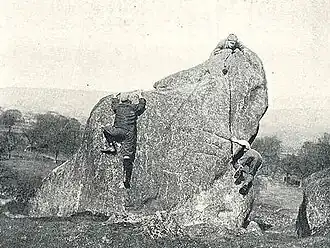 Photo en noir et blanc d'un rocher arrondi d'environ quatre mètres et de personnes l'escaladant.