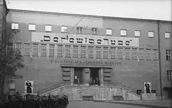 Grand bâtiment public avec inscriptions en allemand et une inscription plus grande qui imite les lettres de l'hébreu.