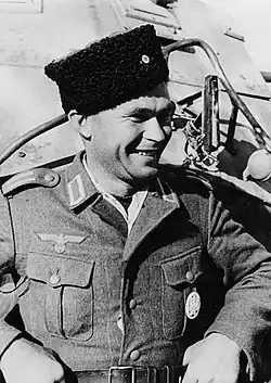 Photo en noir et blanc, en gros plan, d'un homme souriant, Nicolas Balanowski. À droite de sa poitrine figure le Parteiadler. Il porte une coiffe cosaque.