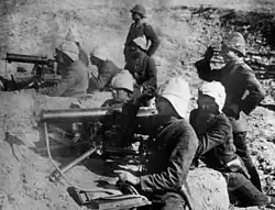 Photographie de deux mitrailleuses disposées derrière un talus et manœuvrées chacune par quatre hommes