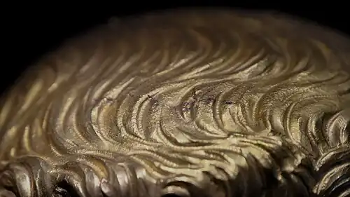 Petites marques grises en forme de vagues sur une surface en or.