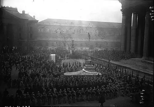 Photographie en noir et blanc d'une foule de soldats entourant deux chars décorés.