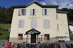 Photographie en couleurs d’un bâtiment de trois étages jaune avec un grillage en bas et des arbres en arrière-plan.