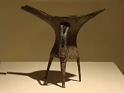 L'évolution des matières et des décors sur une même forme, le tripode jue, au cours de l'âge du Bronze ancien ; de gauche à droite : exemplaires en céramique et en bronze de la période d'Erlitou sans décor, et exemplaire en bronze de la période d'Erligang décoré d'un taotie.