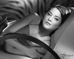 Photographie en noir et blanc d'une jeune femme étendue sur un sofa et regardant l'objectif d'un air impénétrable.