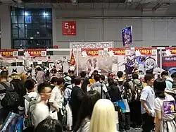 Des personnes font la queue devant différents stands de couleur rouge et montrant des affiches de personnages dessinés.