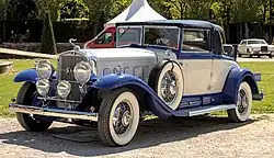 Vue de l'avant-gauche d'une Cadillac V-16 convertible de couleur grise et bleue. Le véhicule est à l'arrêt.
