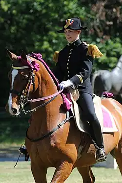 Une femme en uniforme noir assise sur un cheval marron