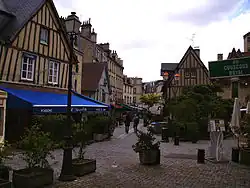 Photographie d'une place de Caen, avec plusieurs commerces, sous un ciel nuageux.