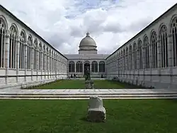 Vaste cloitre. Murs percés fines arcatures gothiques, pelouse centrale. Au fond, un dome