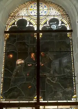 Photographie en couleurs d'un vitrail représentant un corps transporté par des hommes.