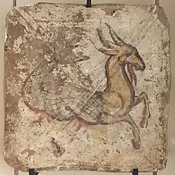 Photo en couleur d'une peinture sur brique représentant une créature avec partie arrière du corps de poisson et partie avant de tête et pattes de chèvre. La créature est peinte en jaune avec contours noirs et des traits rouges orangés donnent du relief