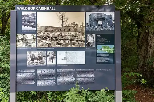 Panneau explicatif pour les visiteurs (2019) qui présentent diverses photos. Dans le sens des aiguilles d'une montre : 1. Vue de 1934, depuis le Wuckersee&nbsp;(de), montrant la Carinhall initiale ; 2. Photo de 1940 avec les travaux en cours pour la seconde extension ; 3. Un passant devant les ruines en 1947 ; 4. Portrait de Göring (1932) en uniforme SA ; 5. Plan de la bande de terre entre les deux lacs, avec la mention des deux extensions de Carinhall (1937 et 1940), Göring avait planifié la fin de la troisième extension (concernant un nouveau musée) pour 1953 ; 6. Plan du projet de cette troisième extension tel que présenté le 12 janvier 1945 ; 7. Visite du général japonais Oshima en mars 1940 ; 8. Göring reçoit le ministre des Affaires étrangères britannique, Lord Halifax, le 20 novembre 1937 ; 9. Le 19 juin 1934, Göring, accompagné de Hitler, sort de la crypte aménagée pour sa défunte épouse Carin, sur la rive nord du Wuckersee&nbsp;(de).