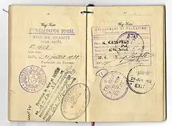 Photographie d'un document au papier jauni, portant plusieurs tampons de plusieurs couleurs, en français et en allemand.